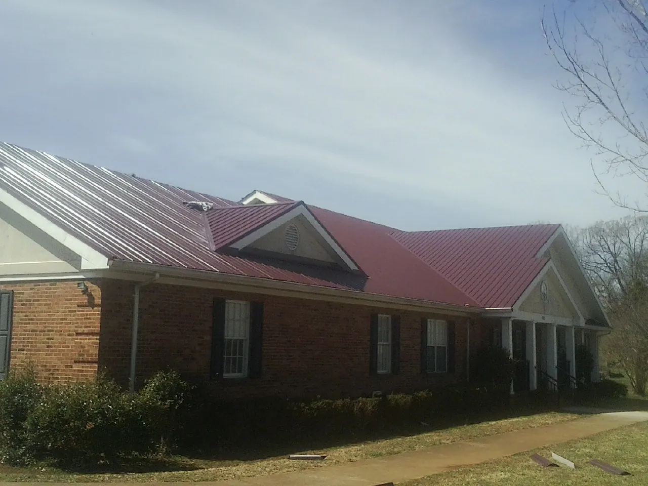 Red metal roof with gabled entries on a long brick building, from a Hail Damage Roof Repair job in Maywood