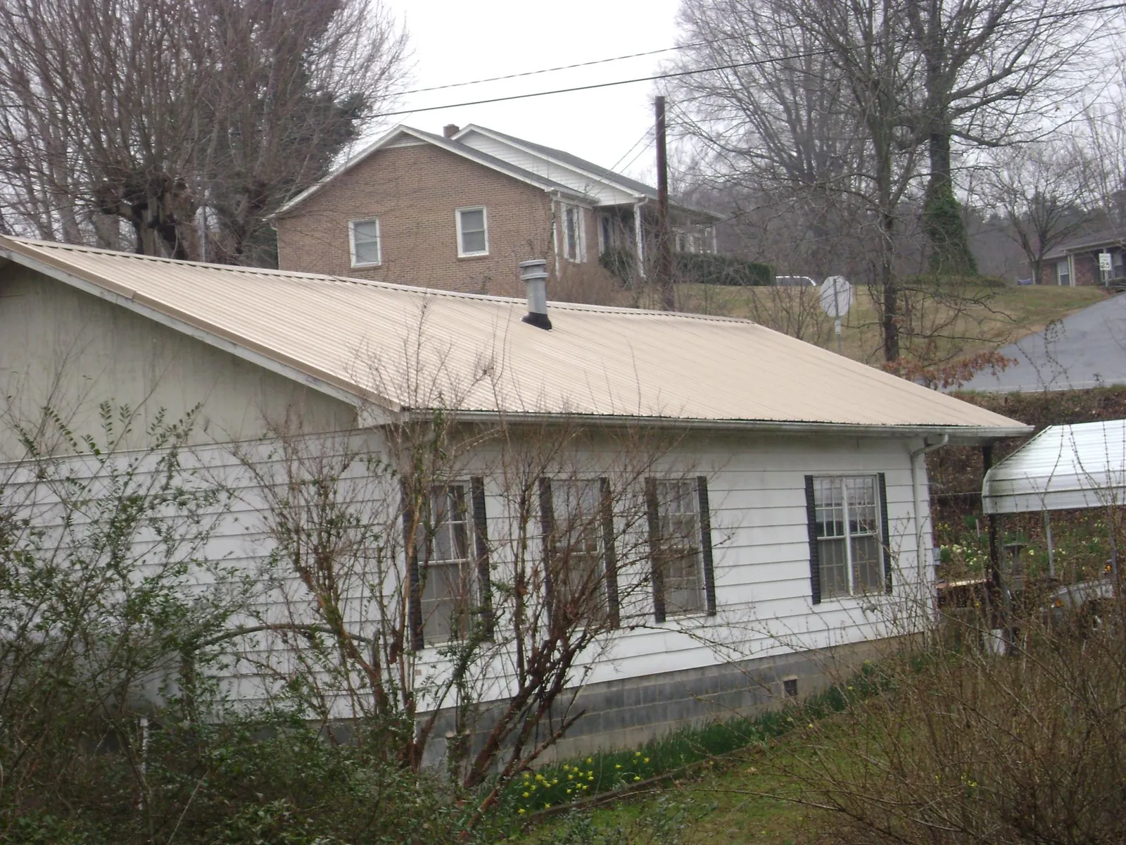 Tan metal roof on a white sided house set into a hillside — Commercial Roofing by Roofing Brothers in Maywood